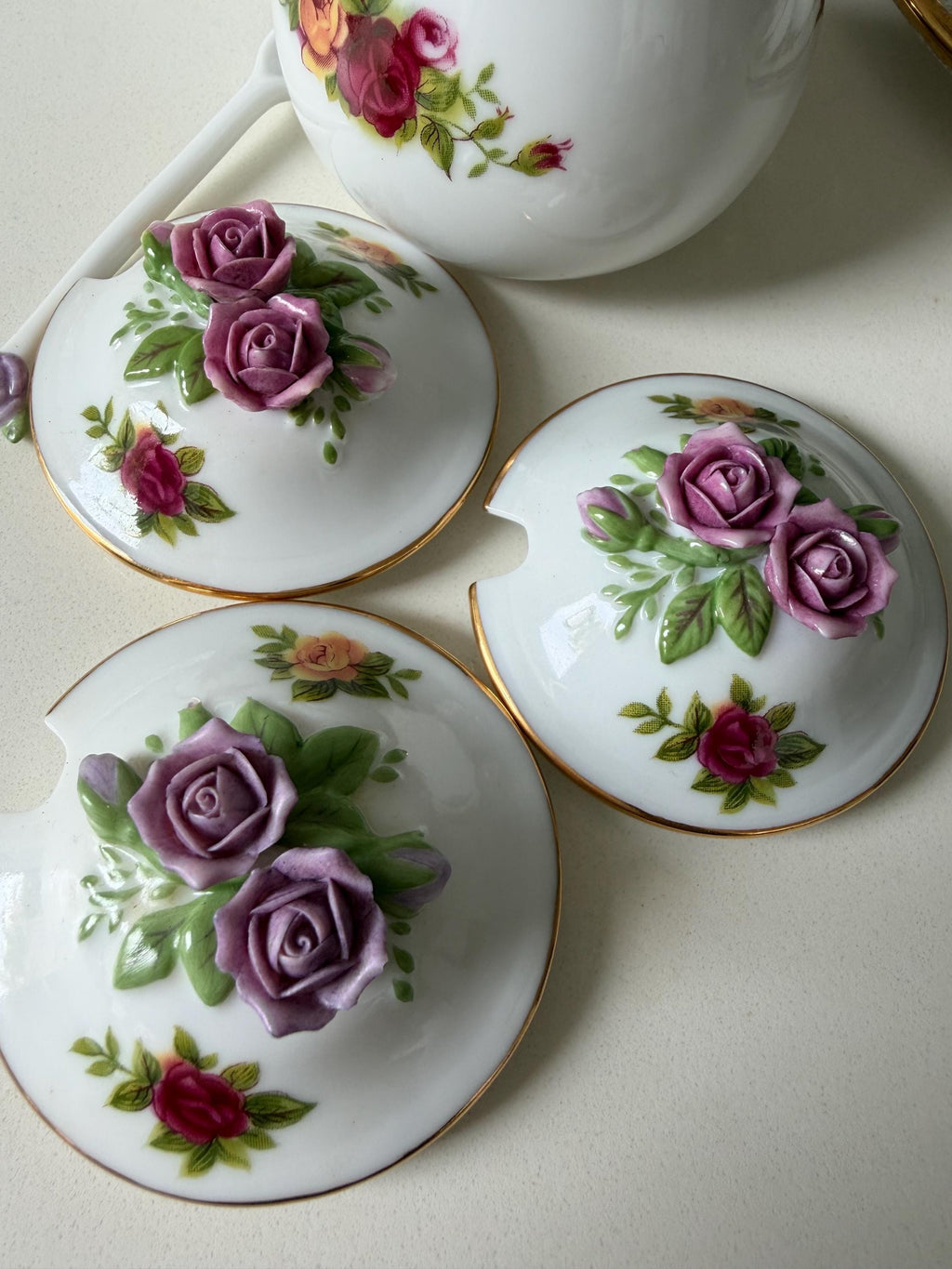 Porcelain jar lids with purple roses, green leaves, and gold trim in a group