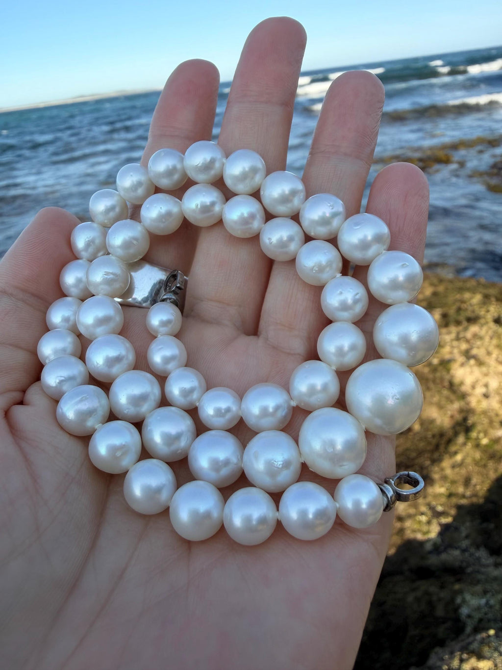 South Sea pearl necklace held in palm with large round white pearls and small metal rings