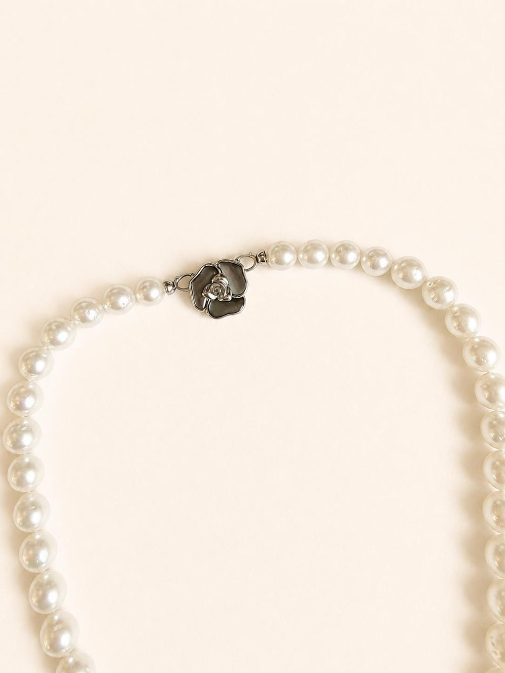 White pearl necklace laid flat with silver-tone clasp at center